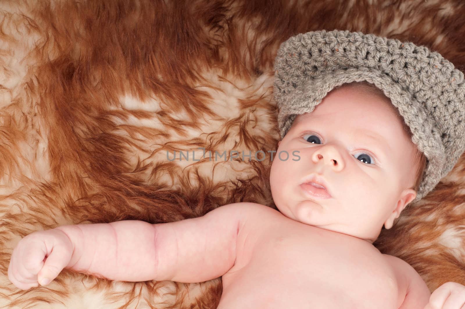 Cute newborn baby in hat lying on fur