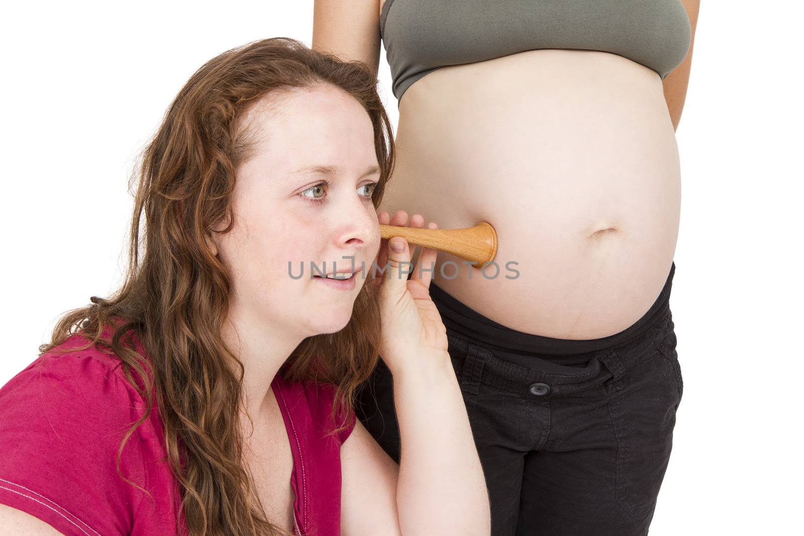 young midwife listening at human belly. pregnant woman standing while midwife is sitting in front. horizontal picture isolated on white