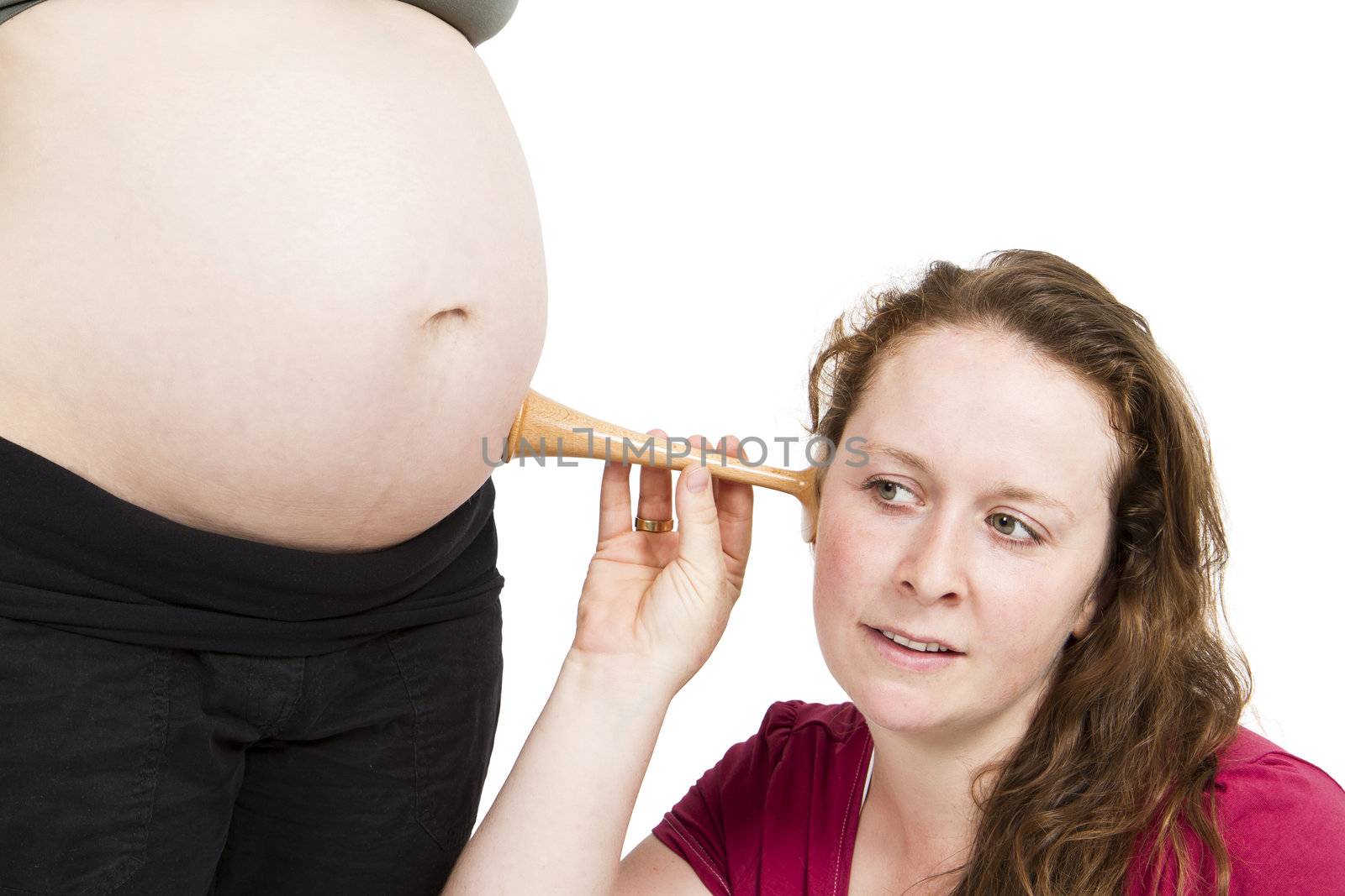 young midwife listening at human belly. pregnant woman standing while midwife is sitting in front. horizontal picture isolated on white