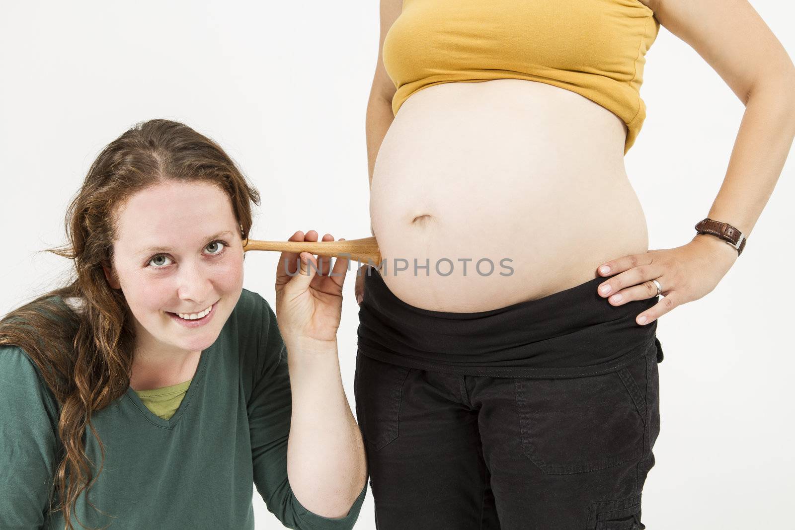 young midwife listening at human belly. pregnant woman standing while midwife is sitting in front. horizontal picture isolated on white