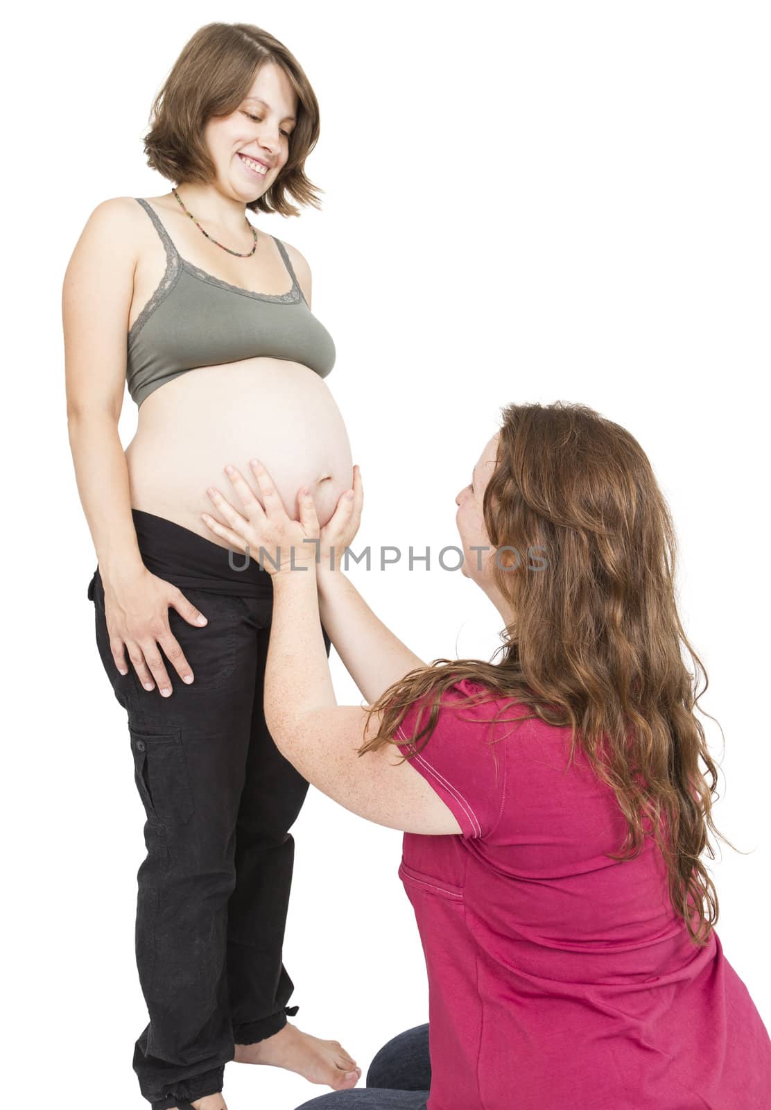 young midwife fingering at human belly. pregnant woman standing while midwife is sitting in front. vertical picture isolated on white