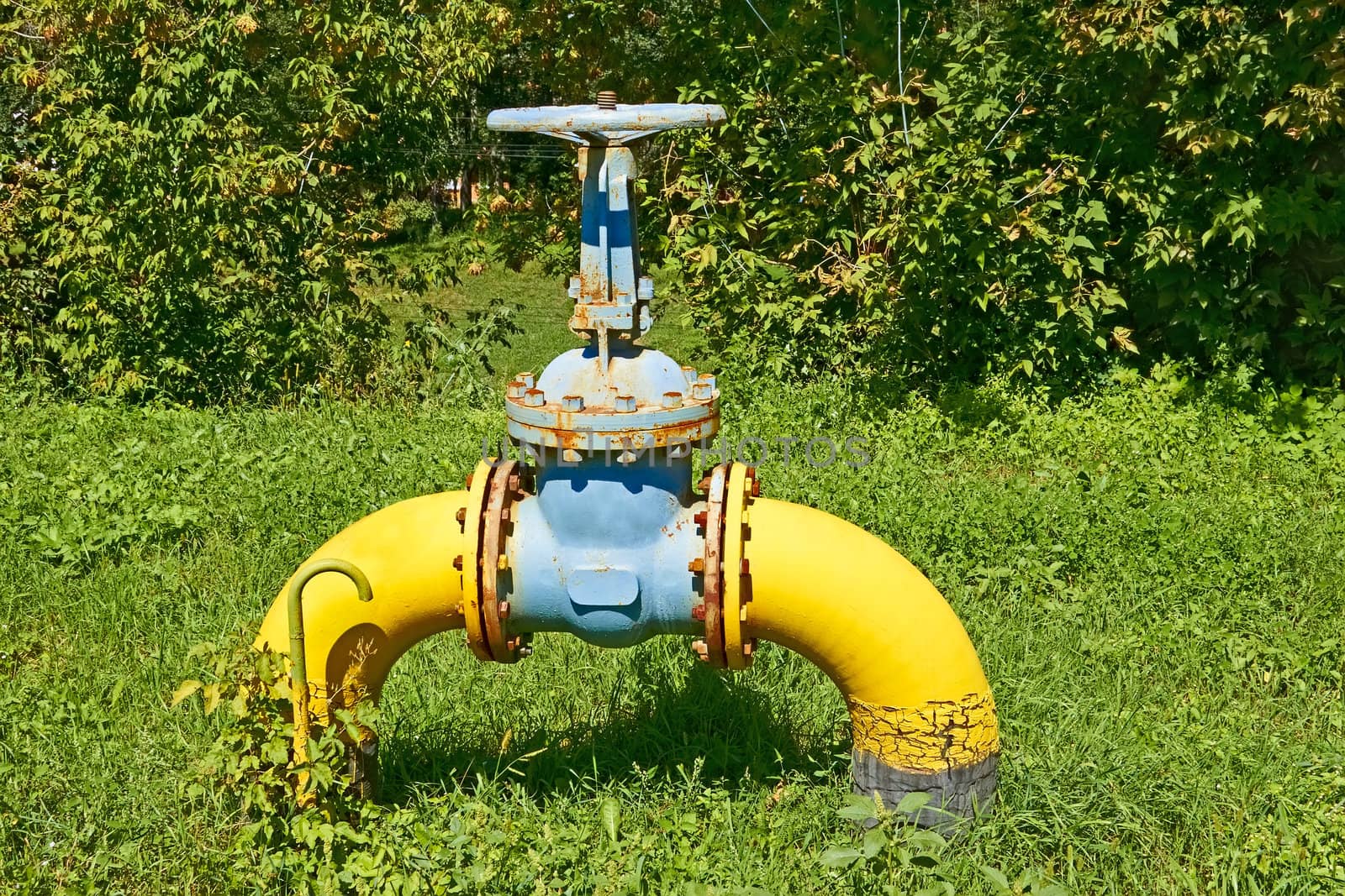 Large gas pipe with a valve and flanges above the ground on against the nature background 