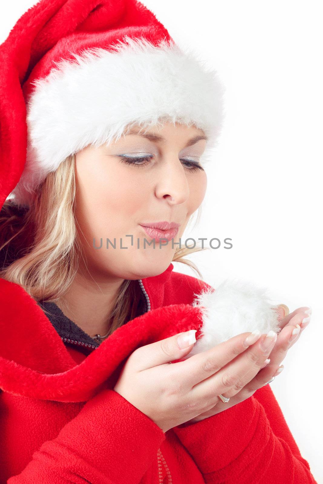 Portrait of joyful pretty woman blowing in red santa claus hat on white background