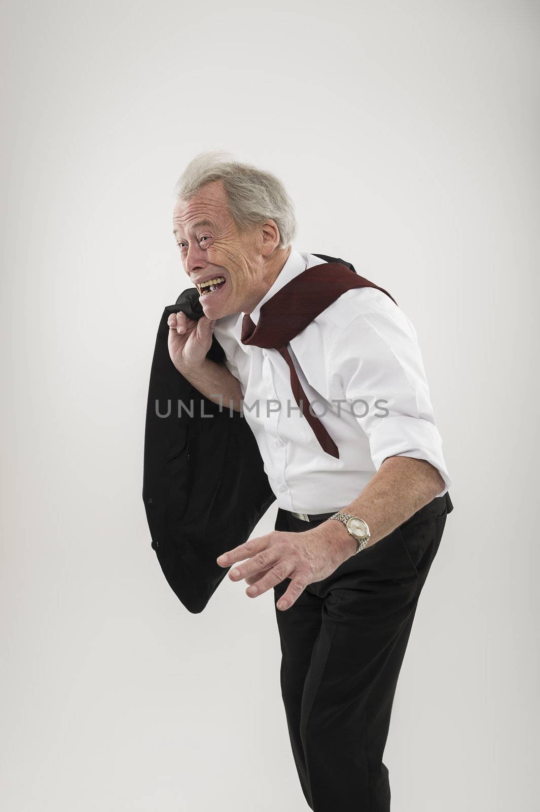 Senior businessman leaning forwards into wind in a stooped stance like an aged man with his tie flapping over his shoulder as he battles the elements, conceptual of business and personal adversity