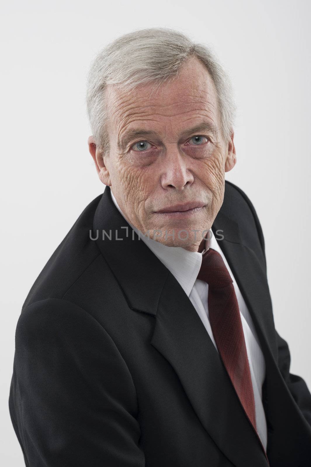 High angle studio portrait of a serious handsome grey haired senior man in a suit and tie looking up at the camera