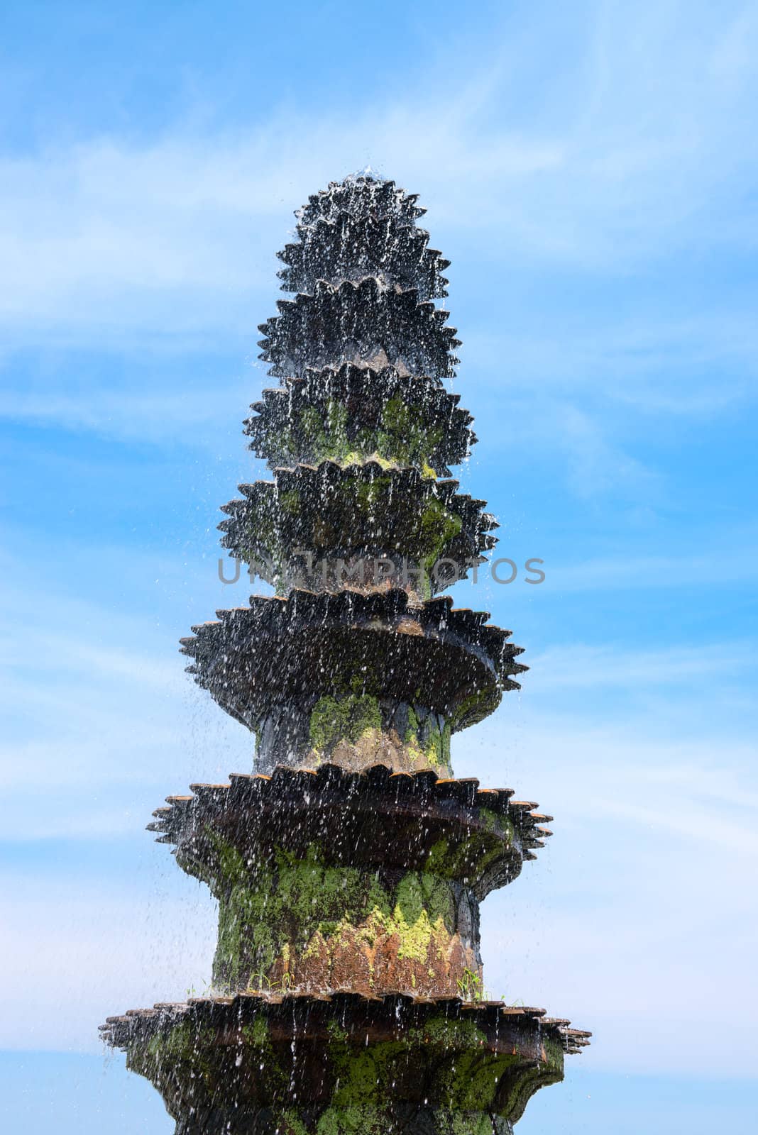 Big old fountain covered by green moss with blue cloudy sky on background