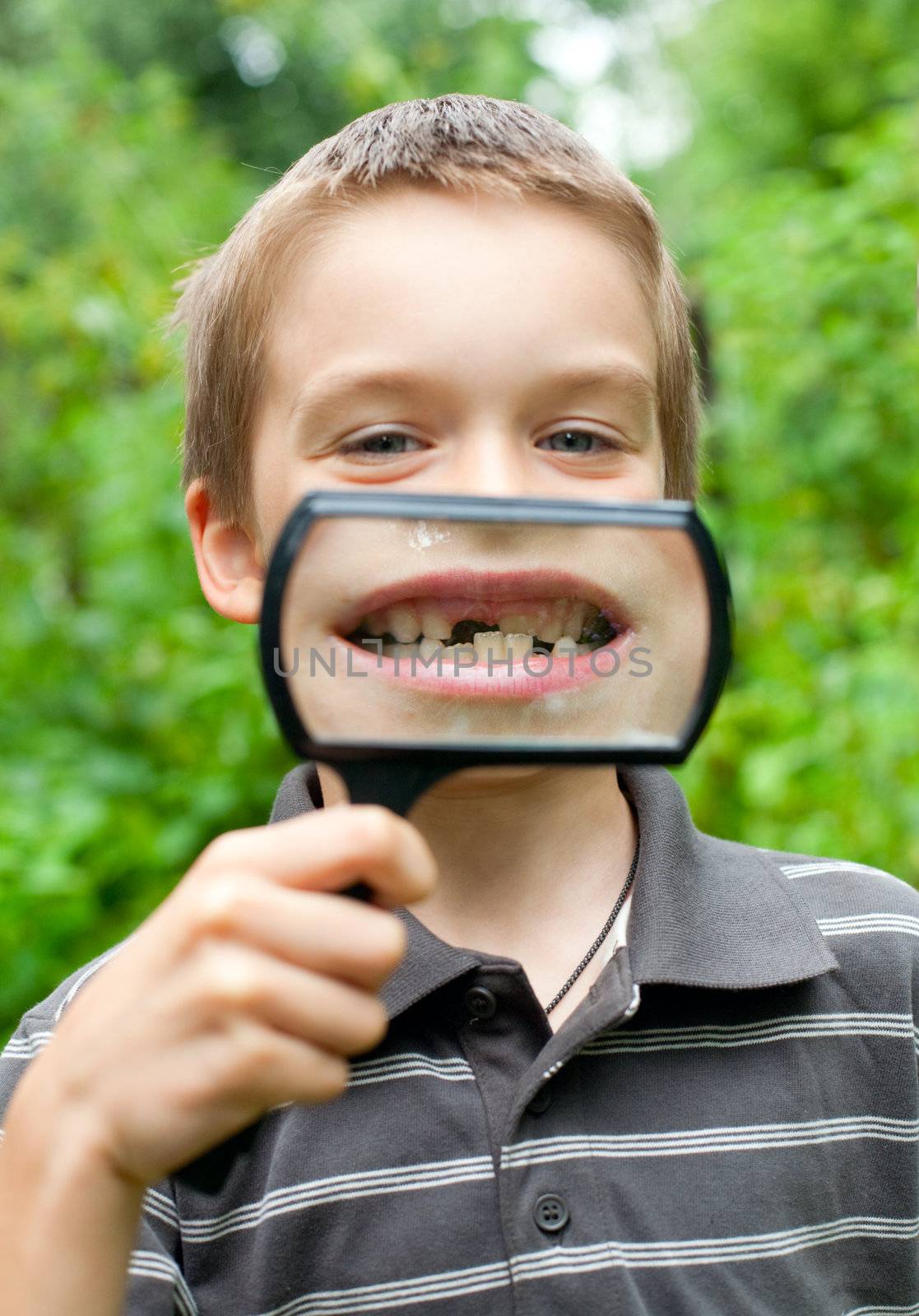 Young boy showing missing baby tooth through hand magnifier, shallow DOF