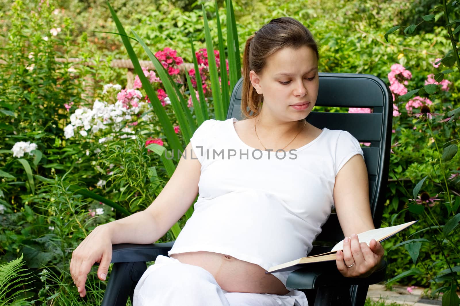 Young pregnant woman reading a book in a summer garden