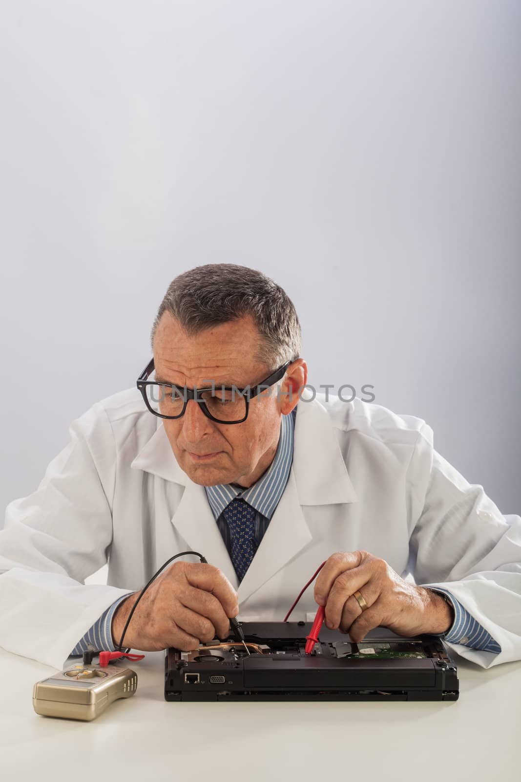 An older male wearing a white lab coat and repairing electronic equipments, like a technician or a repair man.