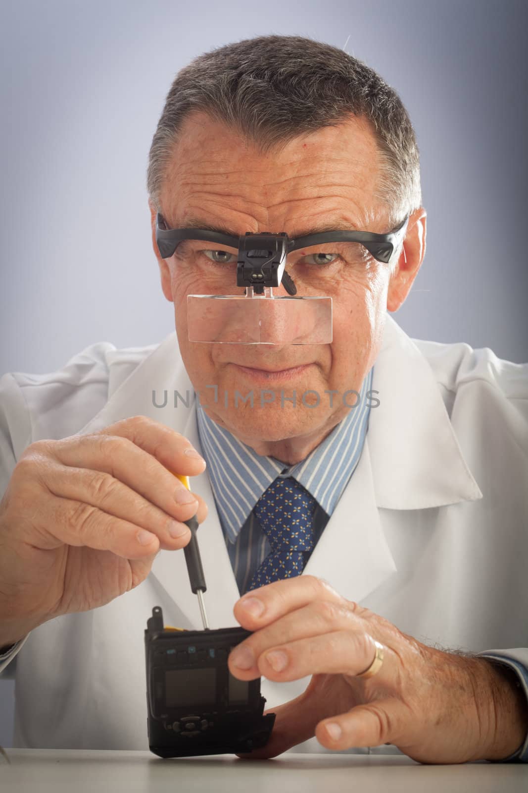 An older male wearing a white lab coat and repairing electronic equipments, like a technician or a repair man.