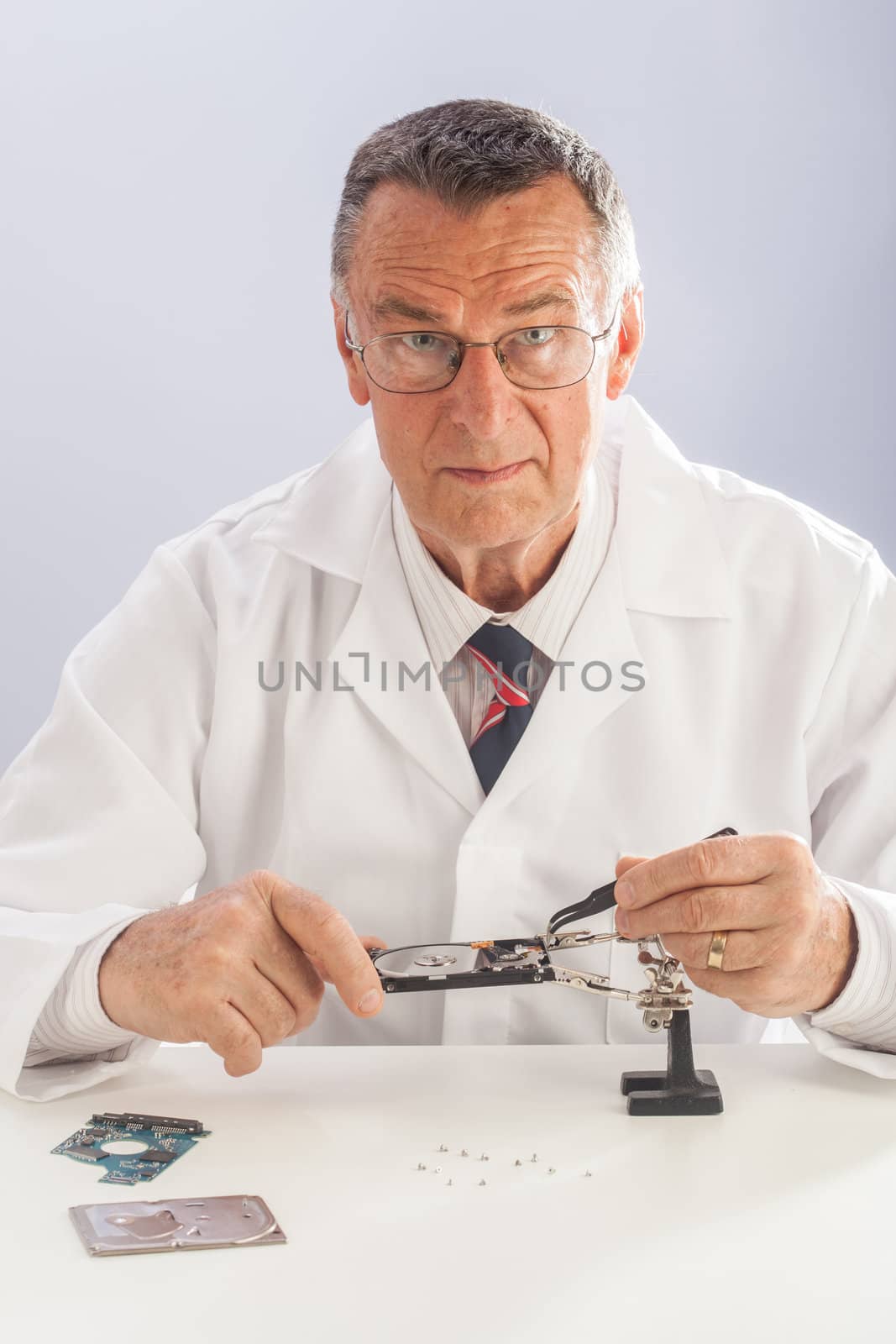 An older male wearing a white lab coat and repairing electronic equipments, like a technician or a repair man.