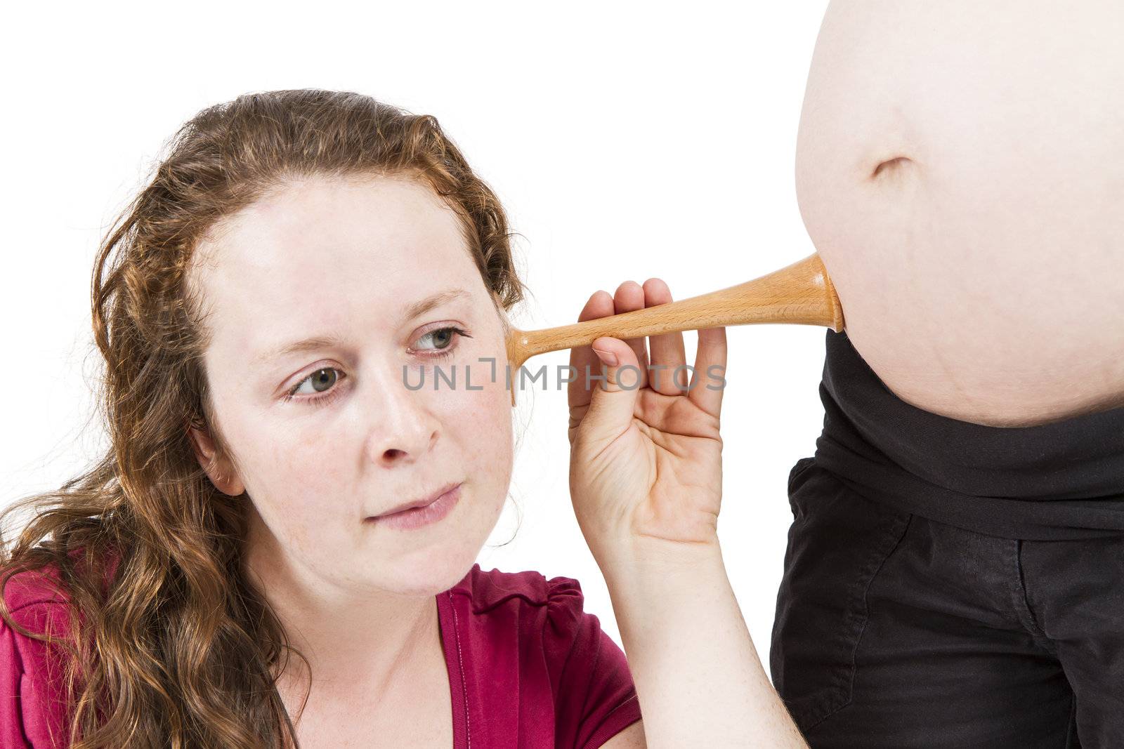 young midwife listening at human belly. pregnant woman standing while midwife is sitting in front. horizontal picture isolated on white