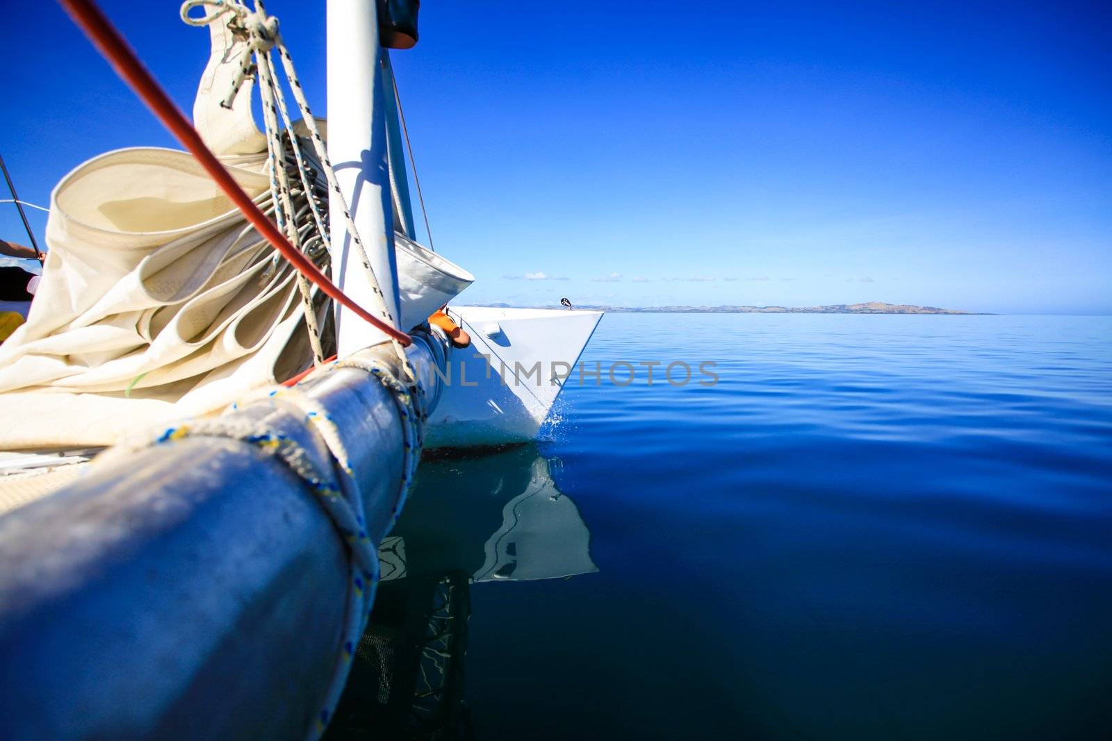 View of the bow of a sailing boat in calm blue sea with red rope riggings and white mast.