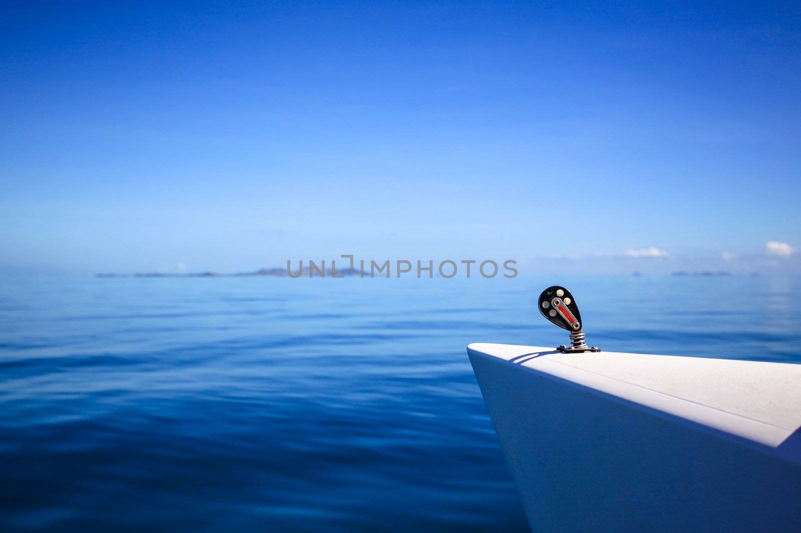 View of the bow of a sailing boat in calm blue sea with red rope riggings and white mast.