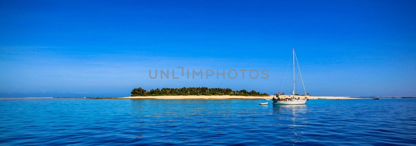 White sailing yacht in front of beautiful Fiji atoll island with white beach in the middle of the ocean.