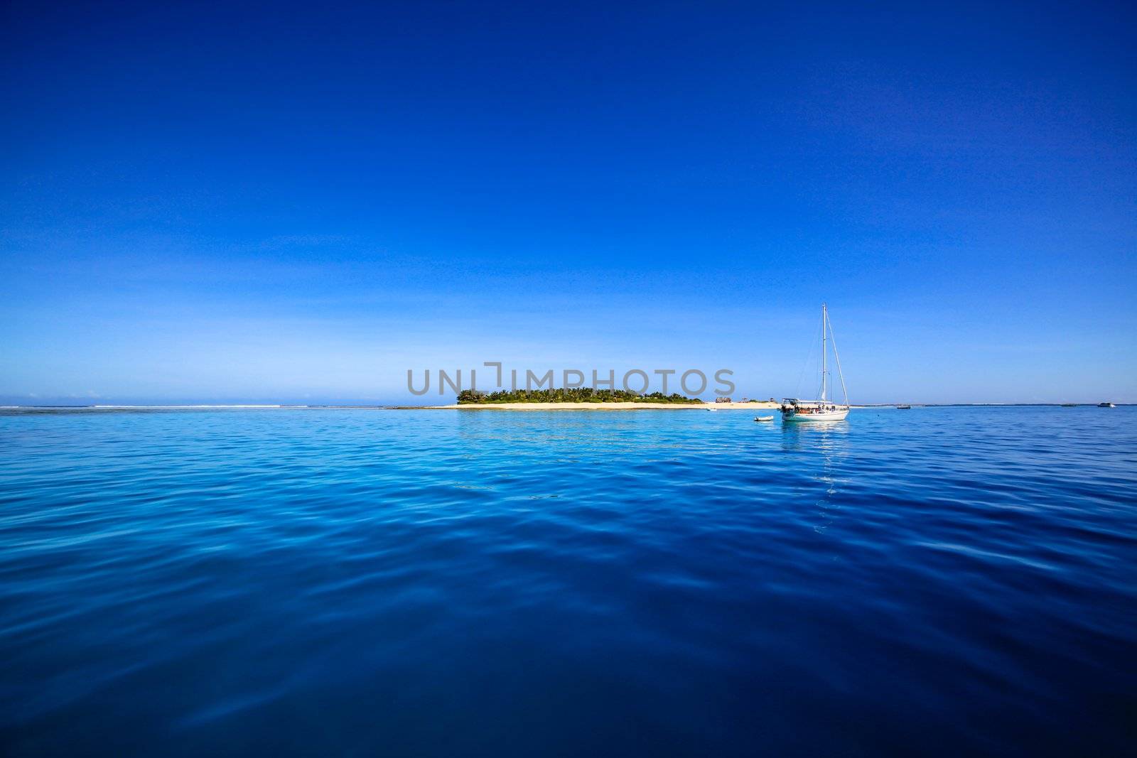 White sailing yacht in front of beautiful Fiji atoll island with white beach in the middle of the ocean.