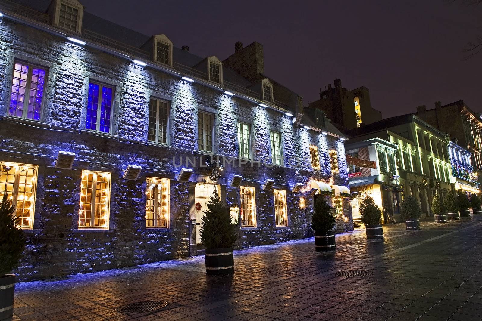 Night scenic of an old, historic stone building with colorful Christmas lighting in the windows - Place Jaques Cartier, Montreal, Quebec, Canada.