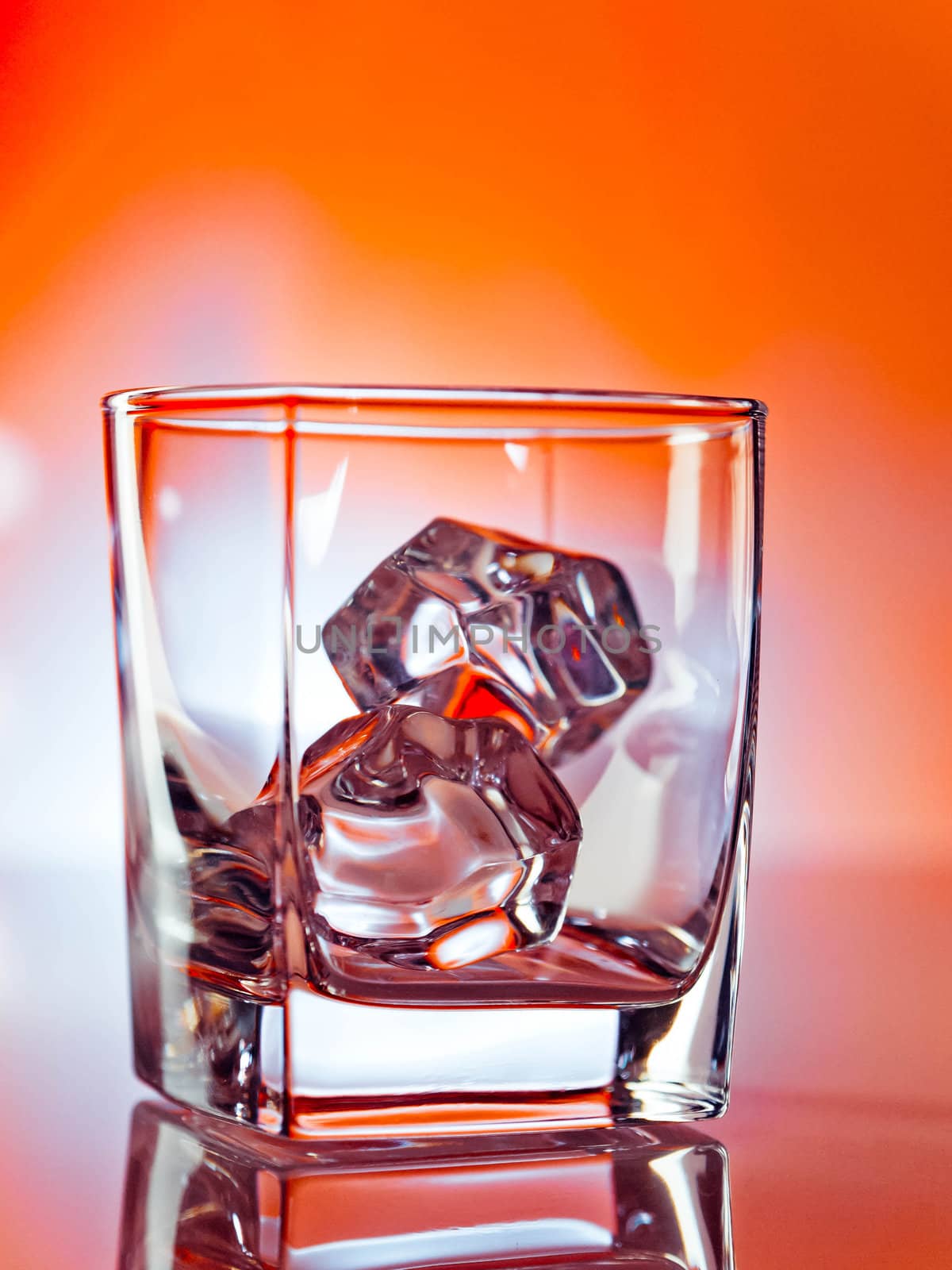 Empty tumbler with two ice cubes over vibrant orange background