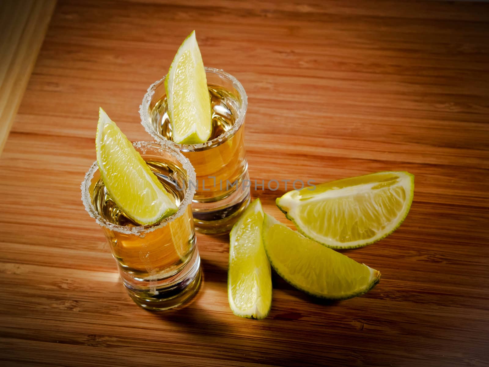 Two tequila shots with salt rims and lime wedges