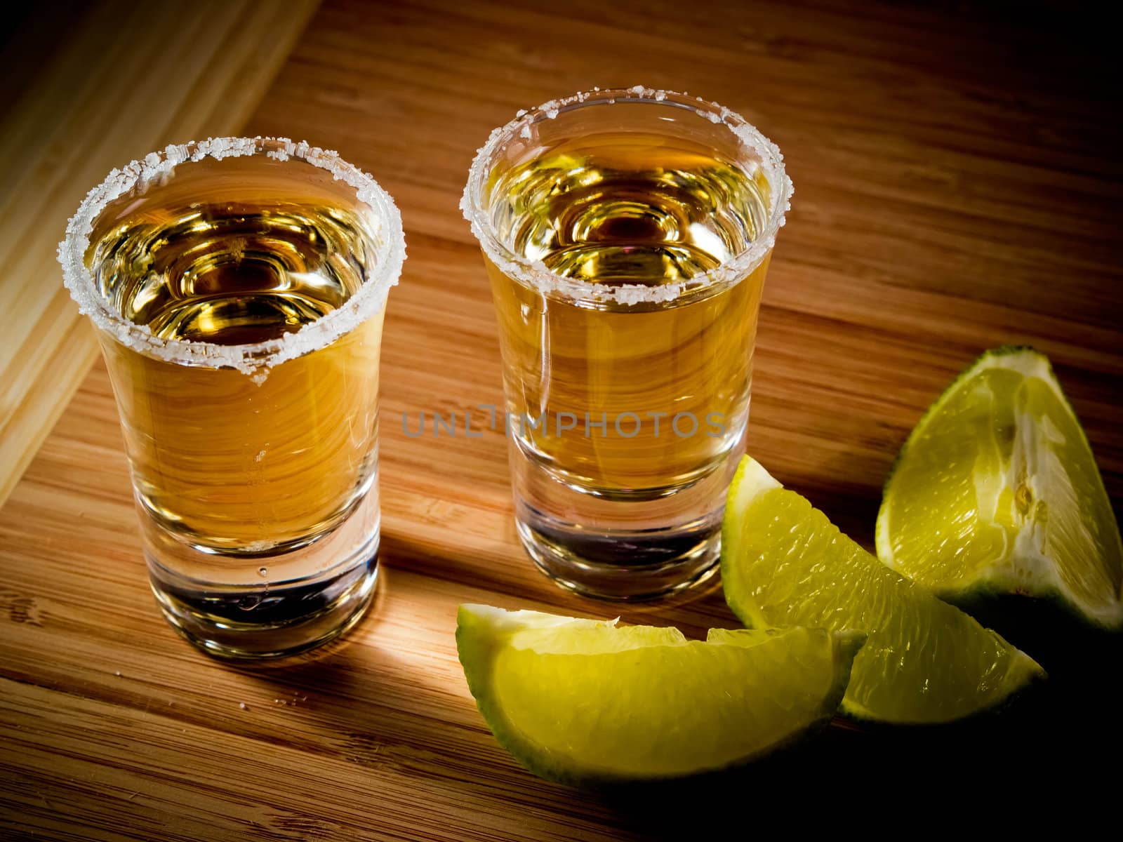 Two shot glasses of tequila with a rim of salt, and lime wedges