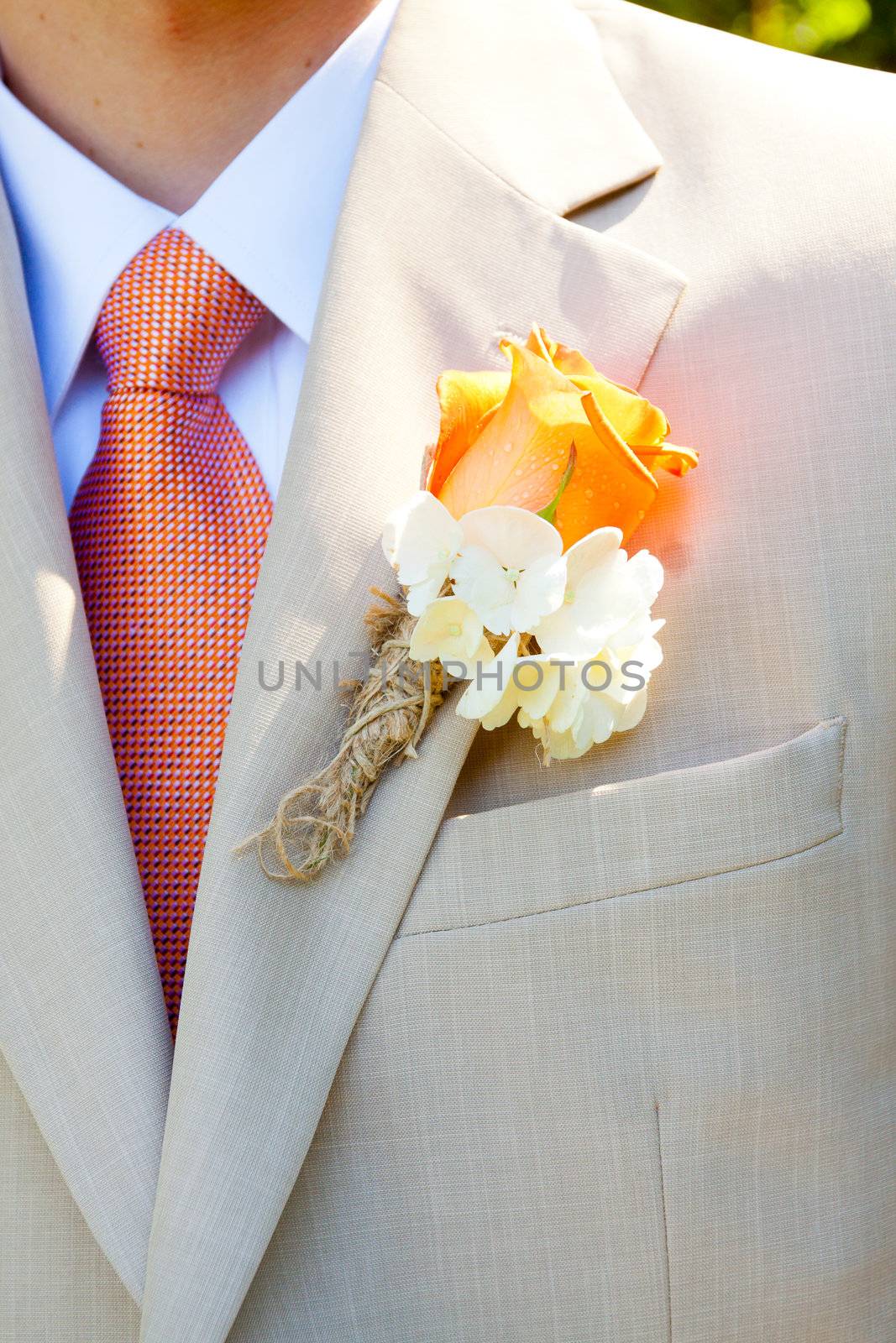 A groom in a light-colored suit is ready for his wedding day in formal attire with a boutineer on his jacket lapel.