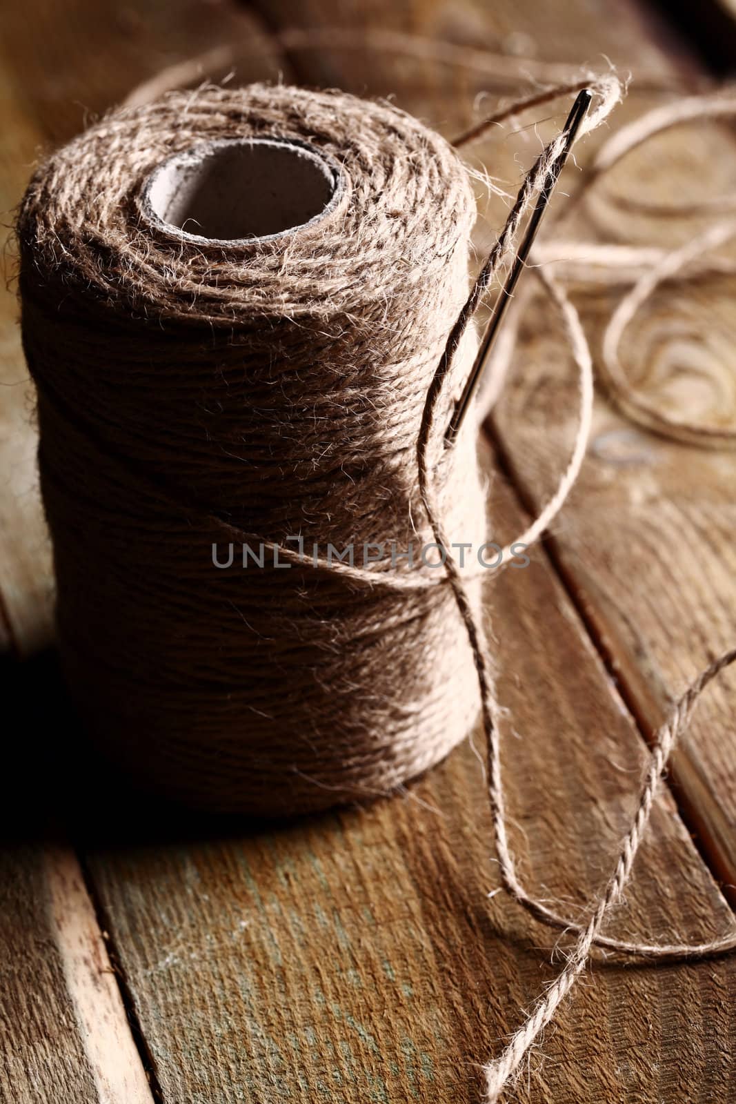 Artistic image of spool of thread and needle over wooden surface