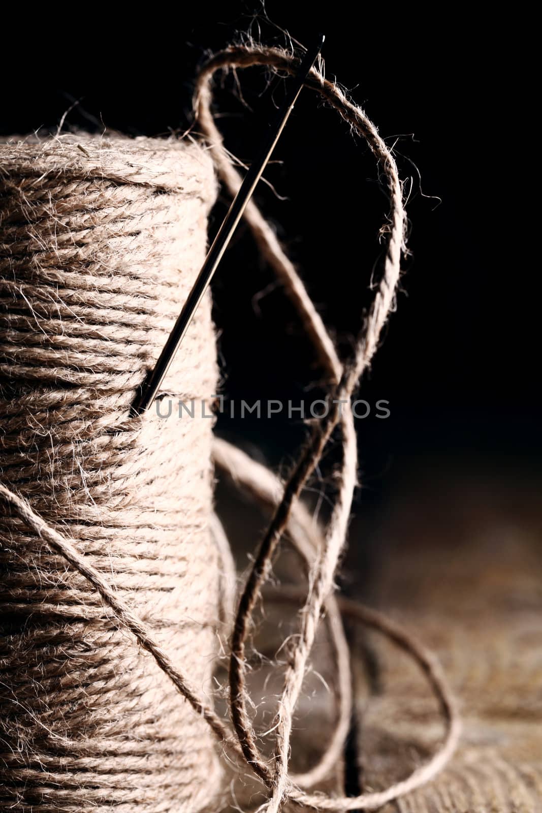 Artistic image of spool of thread and needle over wooden surface