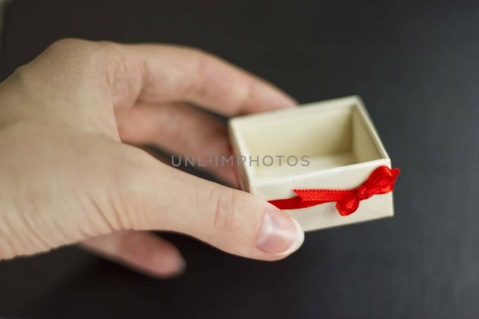 A woman hand holding a white gift box with red ribbon. Black background
