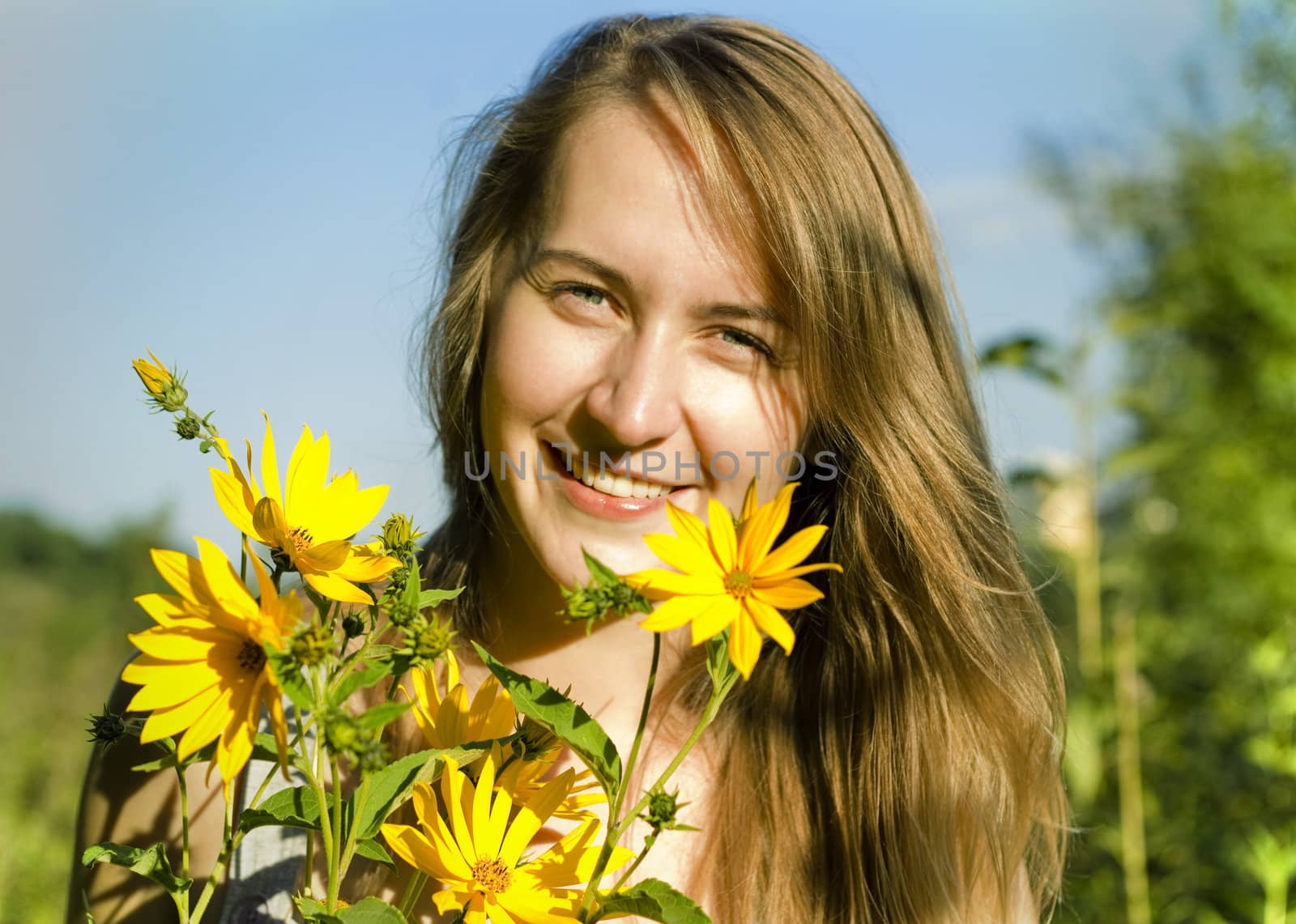 Smiling blond young woman with yellow flowers in a summer nature background