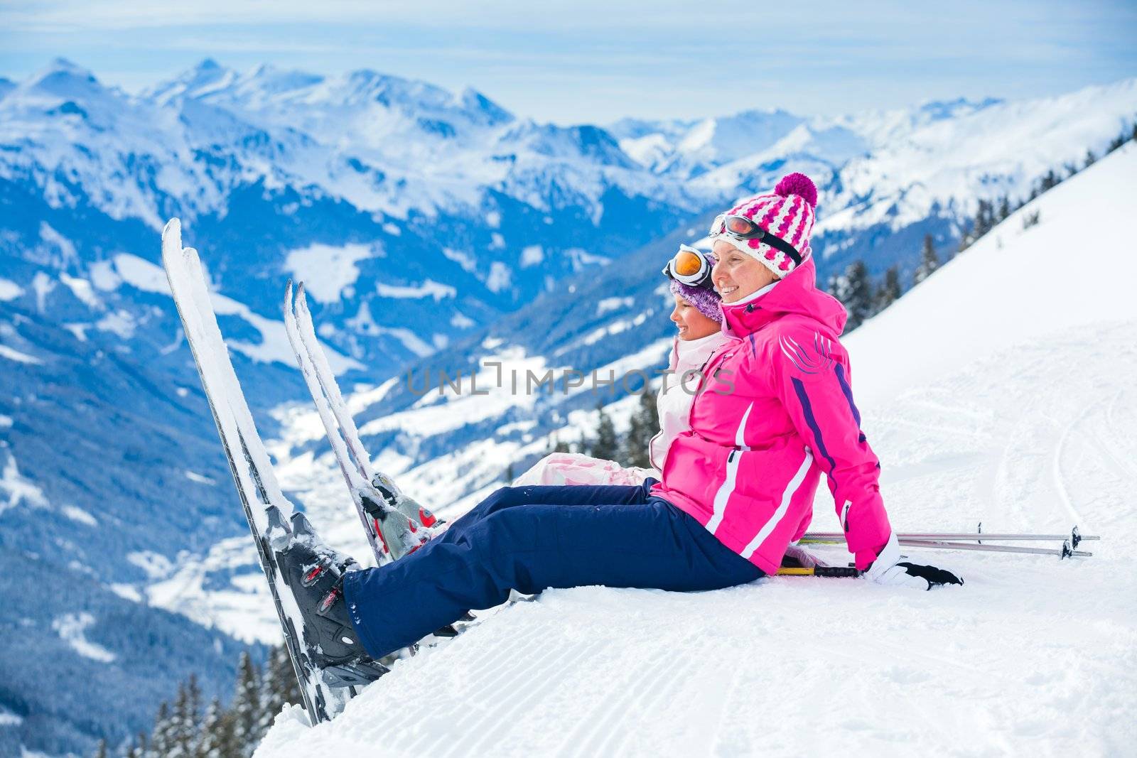 Young girl with her mother in a ski outfit sitting on the snowy hill in the Zillertal Arena, Austria