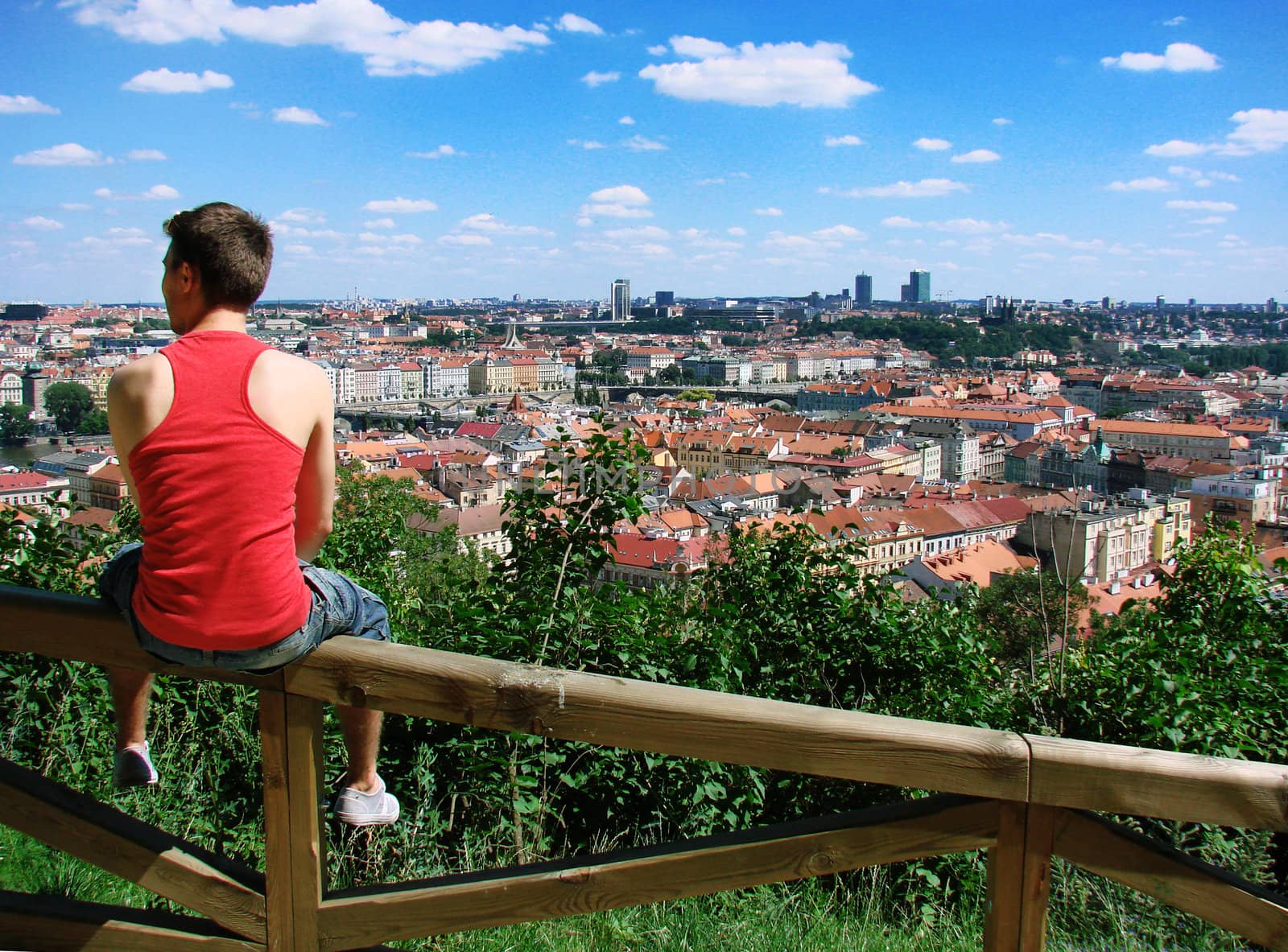 A guy sitting on a fence against panorama of the city