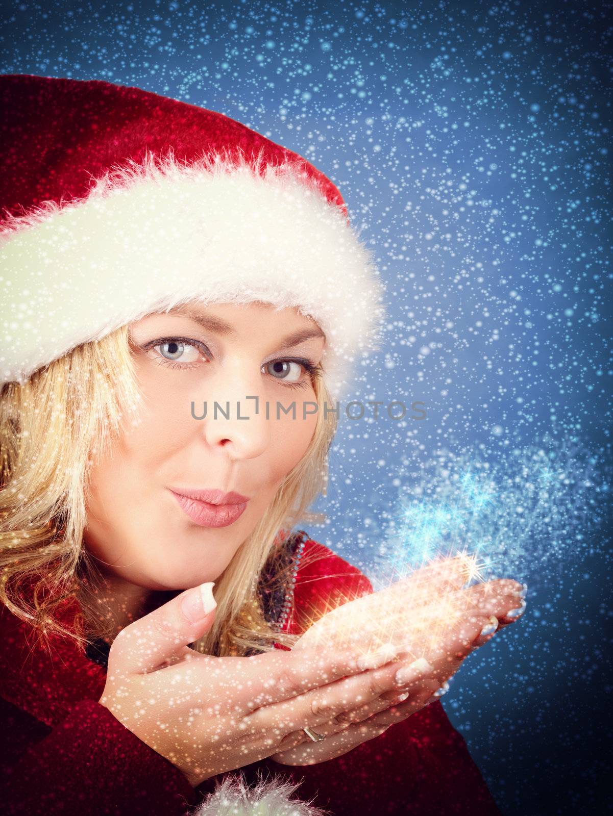 Joyful pretty woman blowing stars in red santa claus hat on snowy blue background