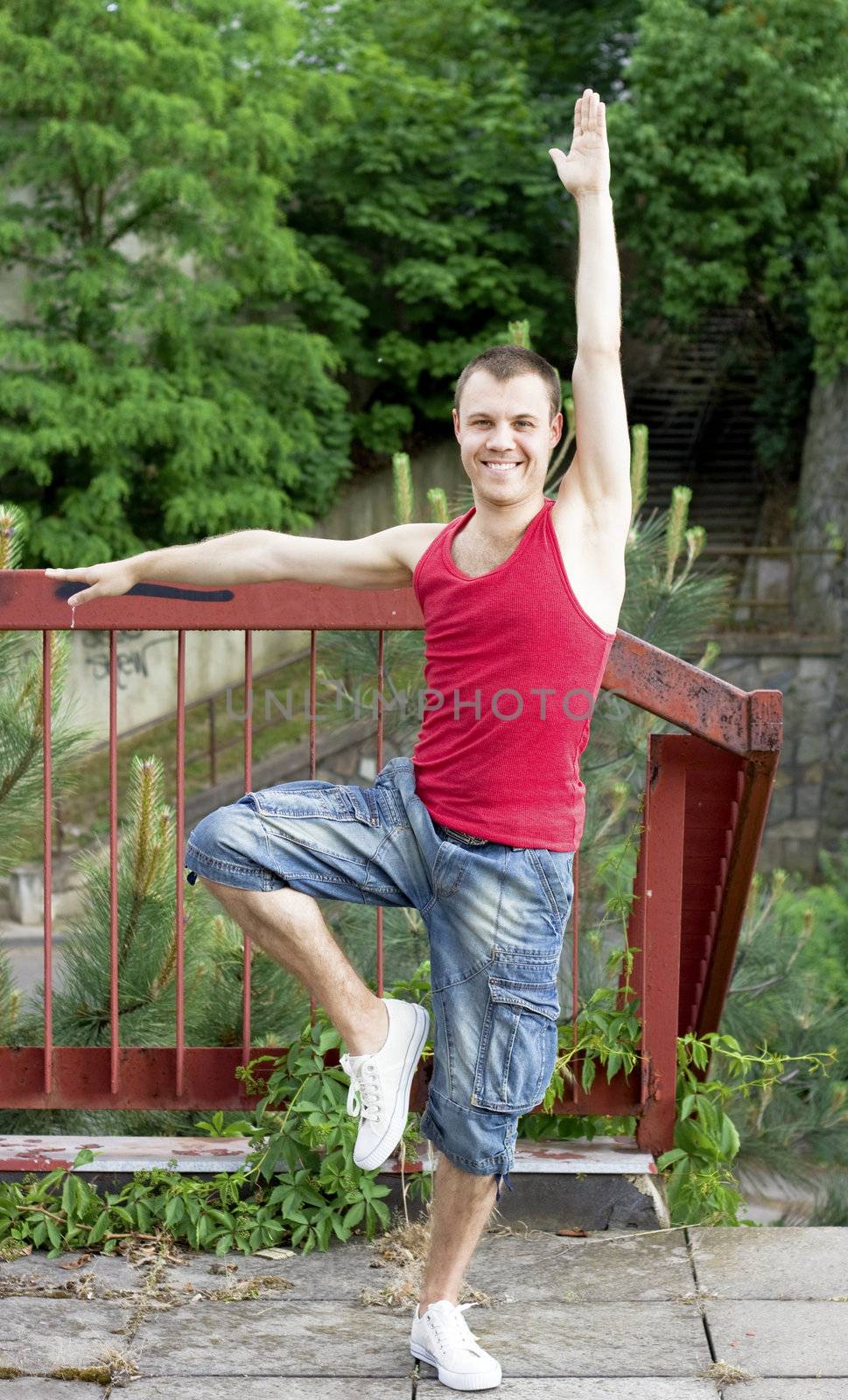 A smiling guy doing gymnastics, outdoors background