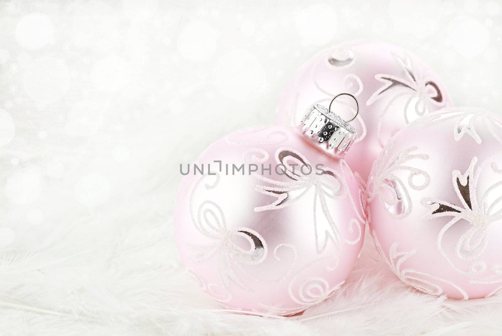 Macro of pink Christmas ornamets lying on a background of white feathers. Extreme shallow depth of field.