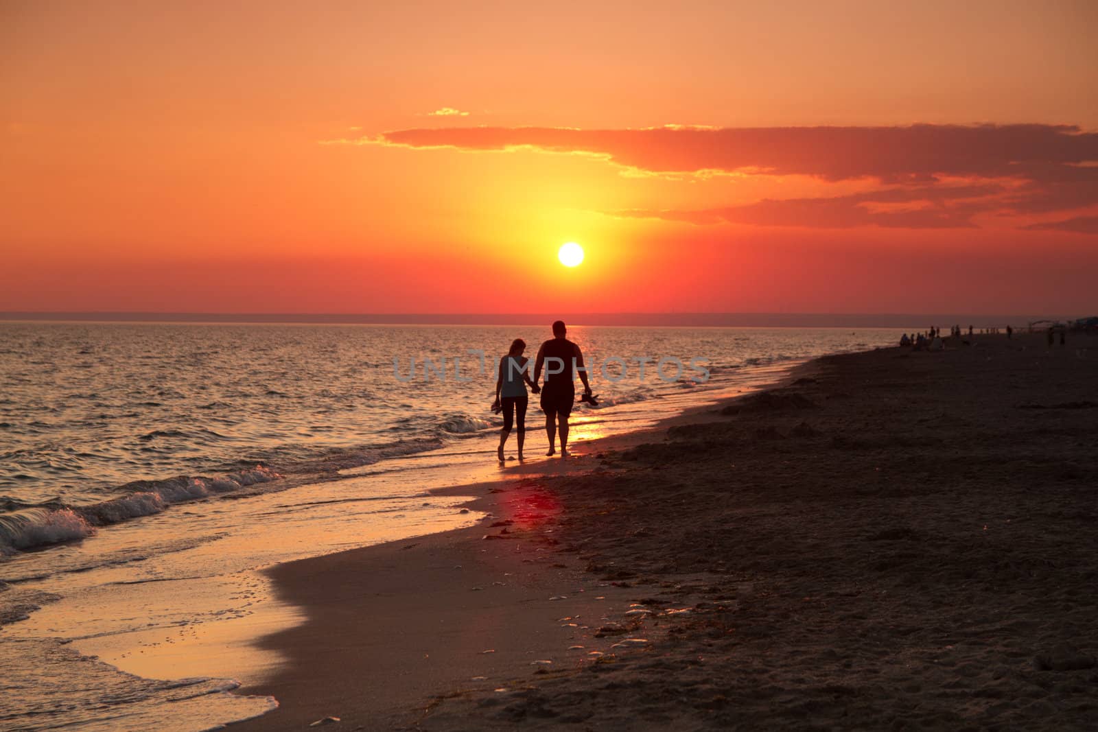 girl with a man walking on the beach admires the sunset by the sea
