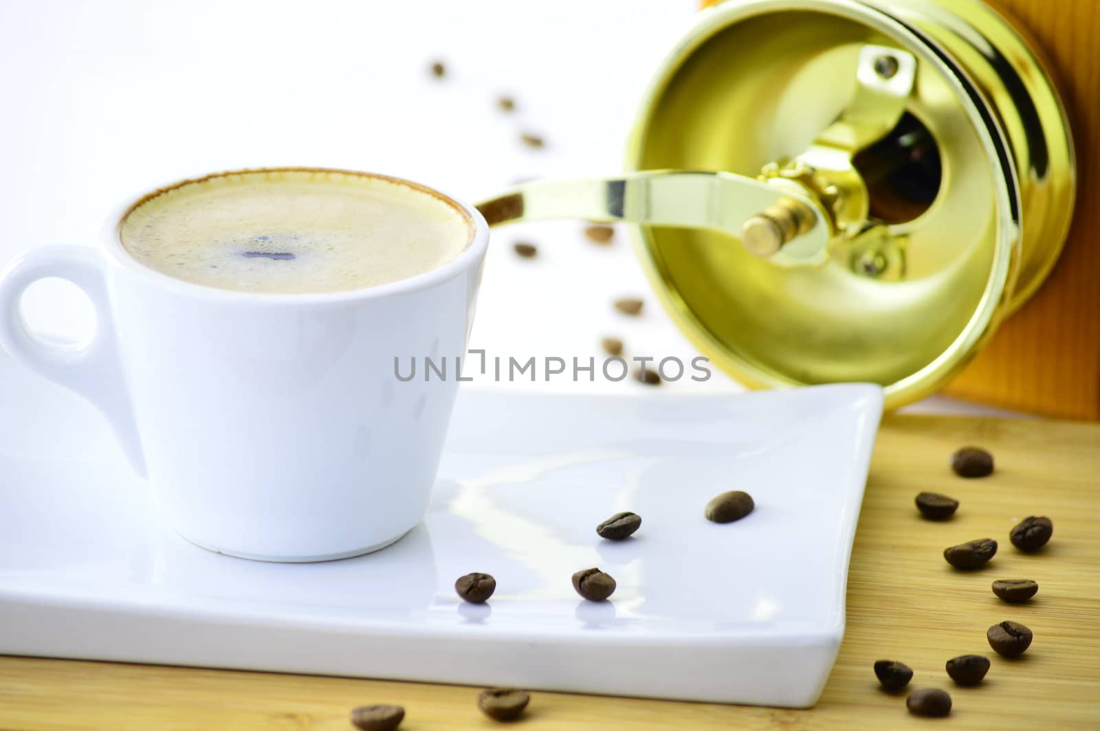 white cup of coffee on a plate in front of a coffee grinder