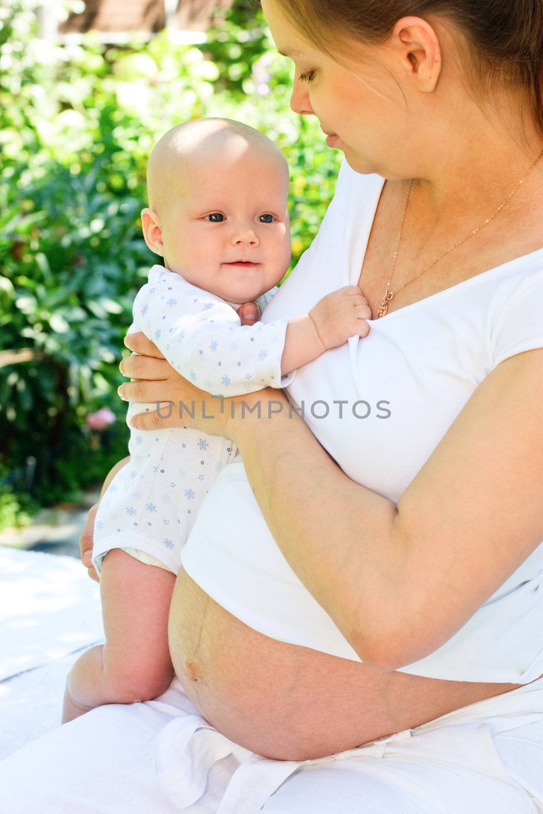 Young pregnant woman holding baby girl in a summer garden