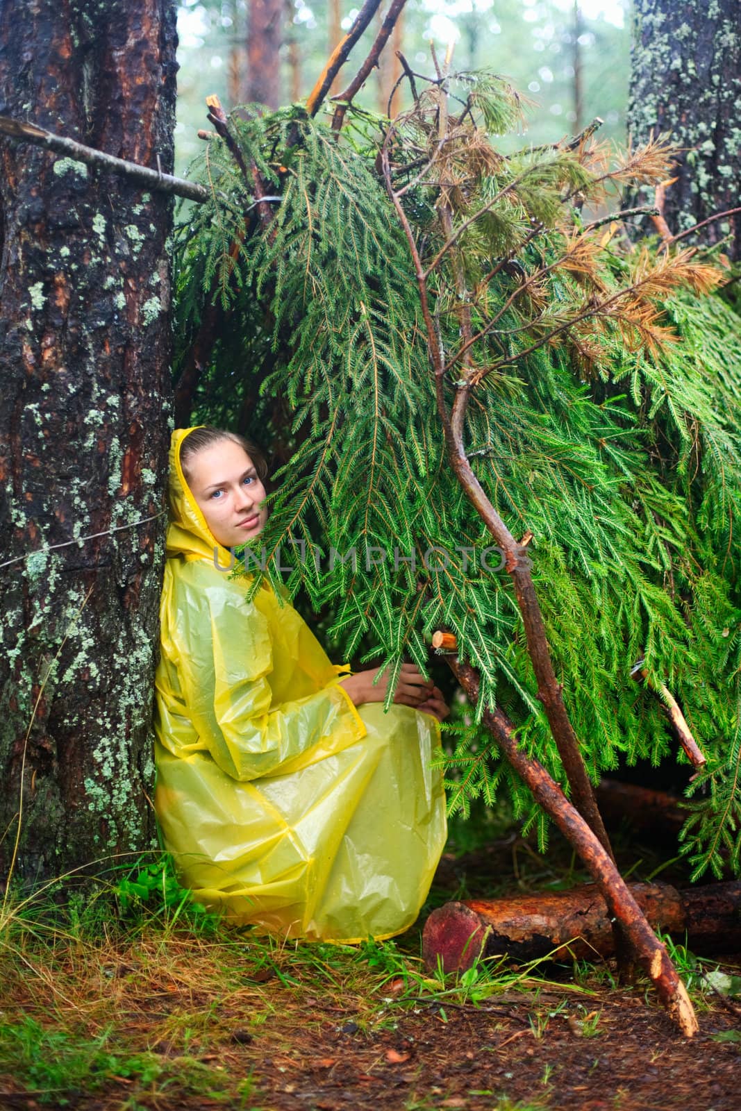 Young woman wearing yellow raincoat sitting in a shelter of branches