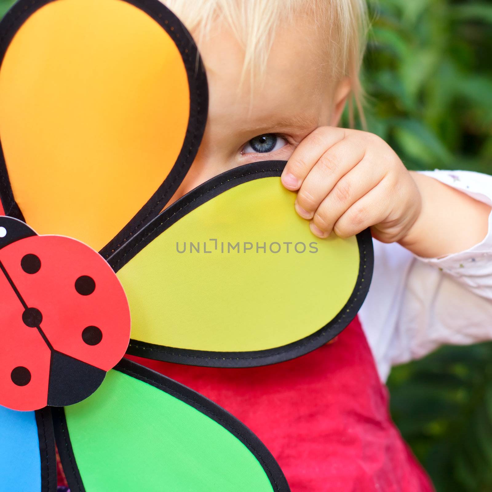 Portrait of cute little girl hiding behind flower toy outdoors