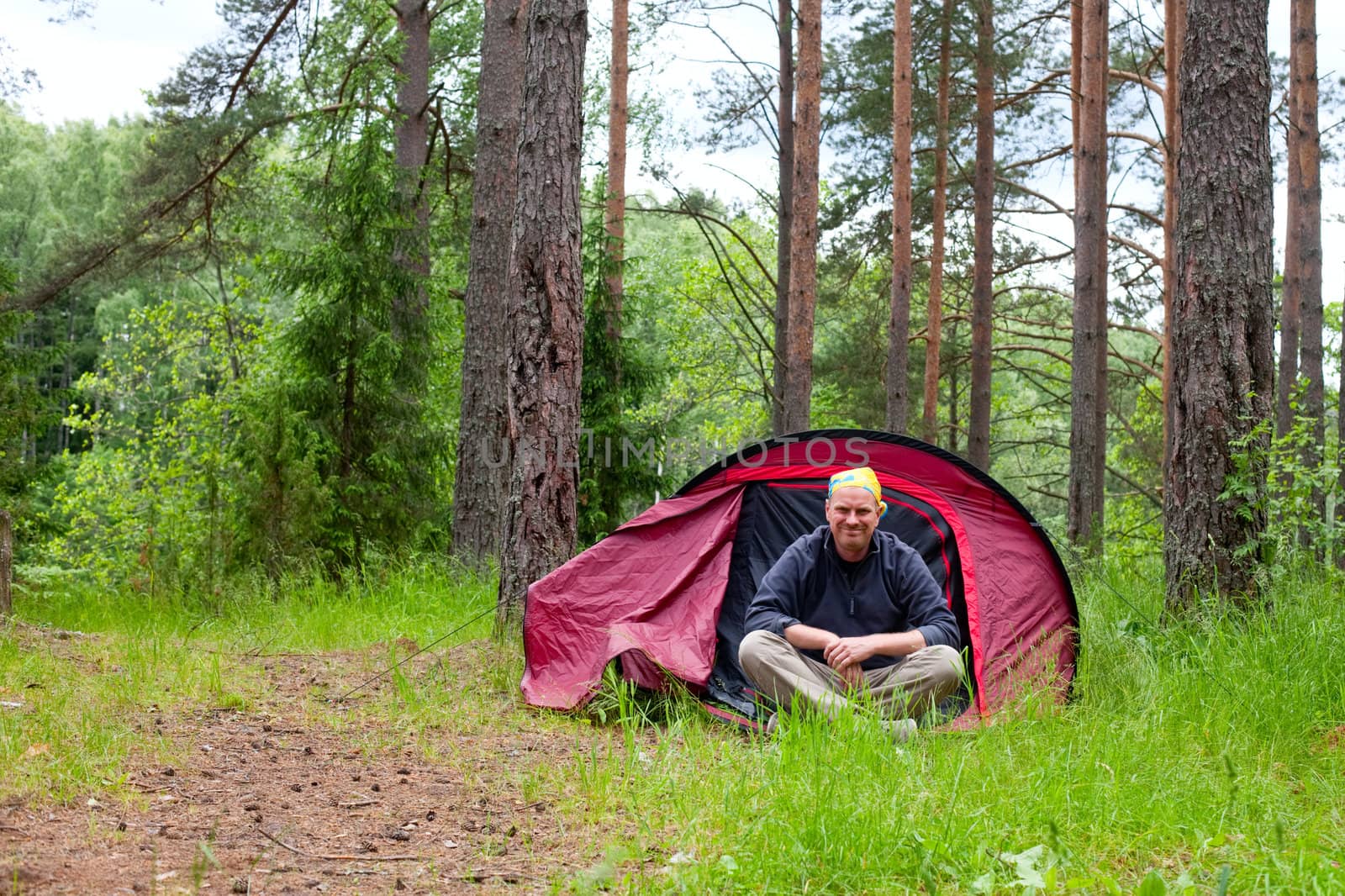 Cheerful tourist sitting in red tent in a forest