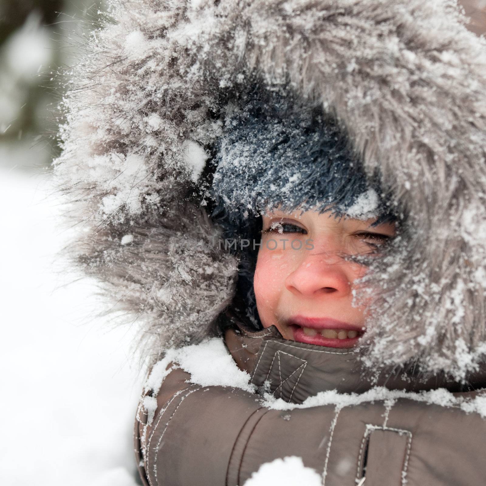Young boy wearing winter jacket with furry hood playing in snow