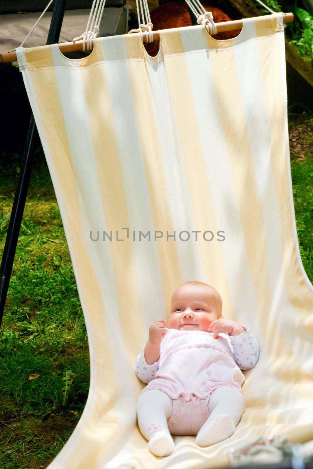Baby girl in lying in the striped hammock on a summer day