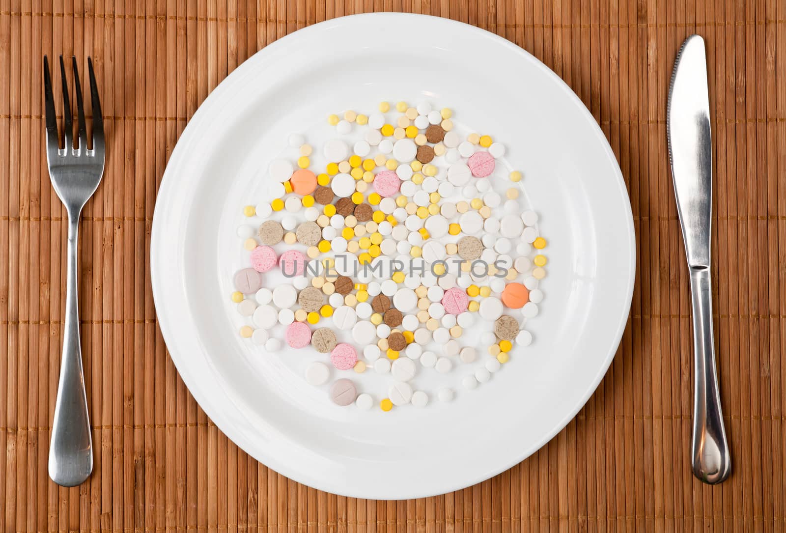 White plate with pills fork and knife on bamboo mat