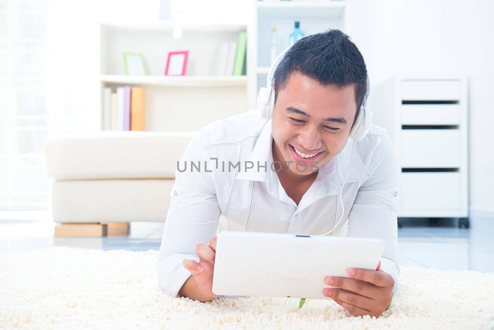 Asian man listen mp3 with headphone, lying on floor at home.