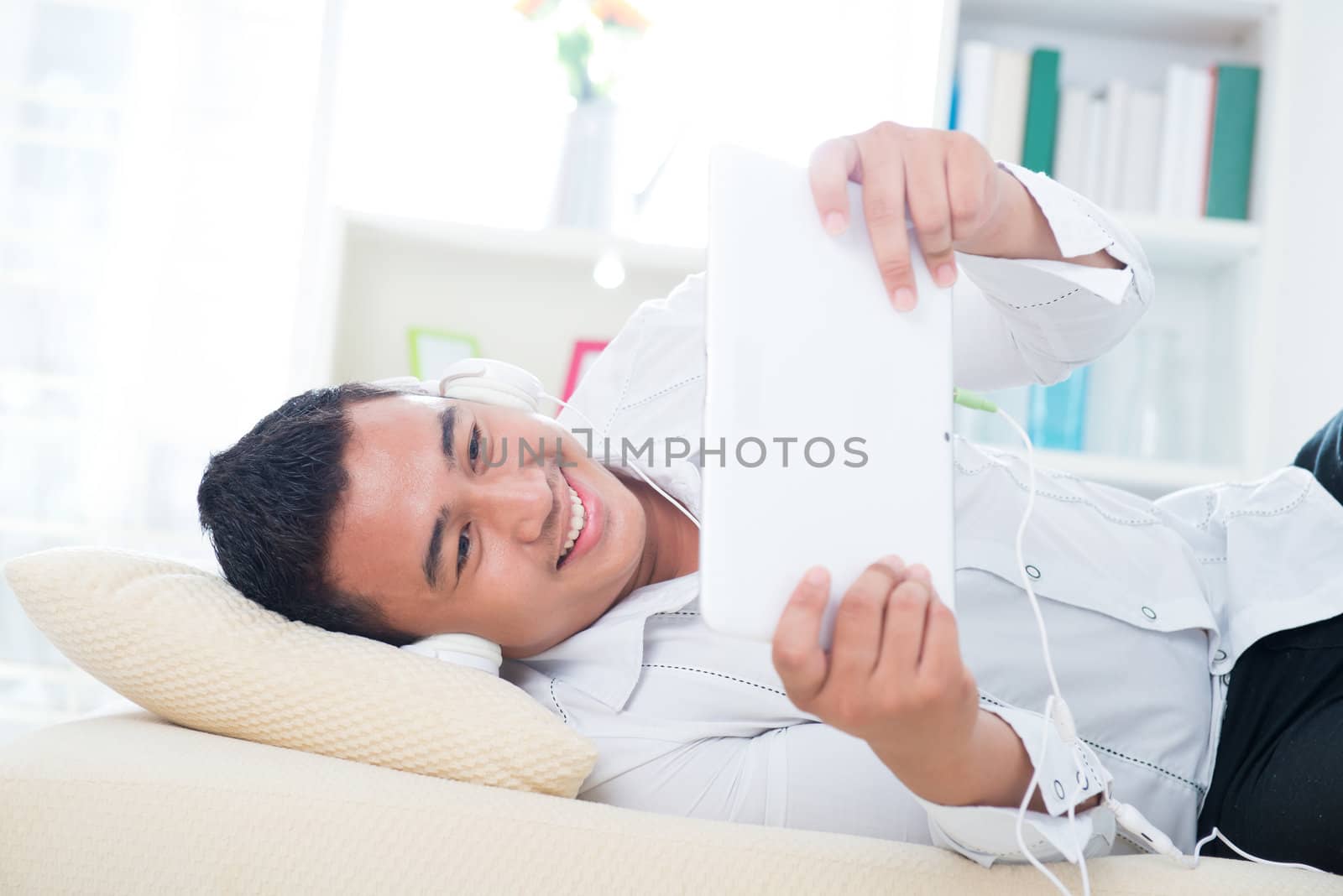 Asian man listen song with headphone, lying on sofa at home.