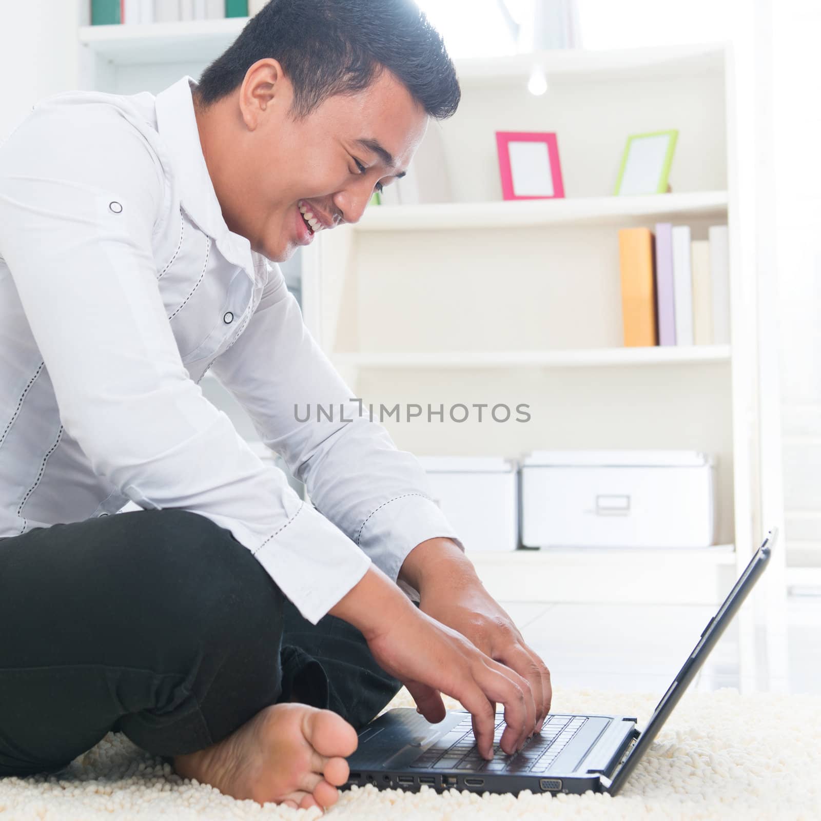 Southeast Asian man surfing internet at home, sitting on floor.