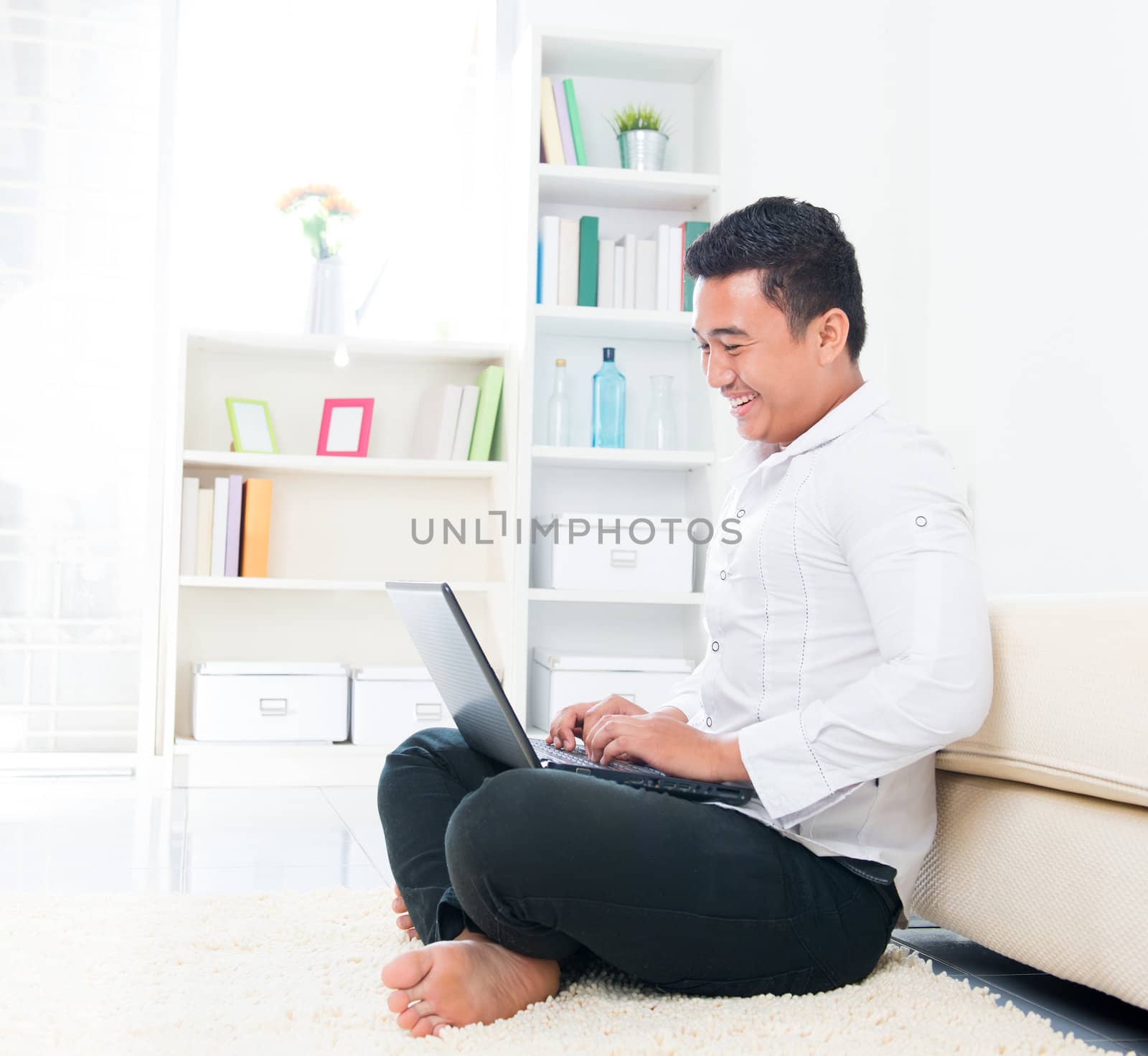 Asian man browsing internet at home, sitting on floor.