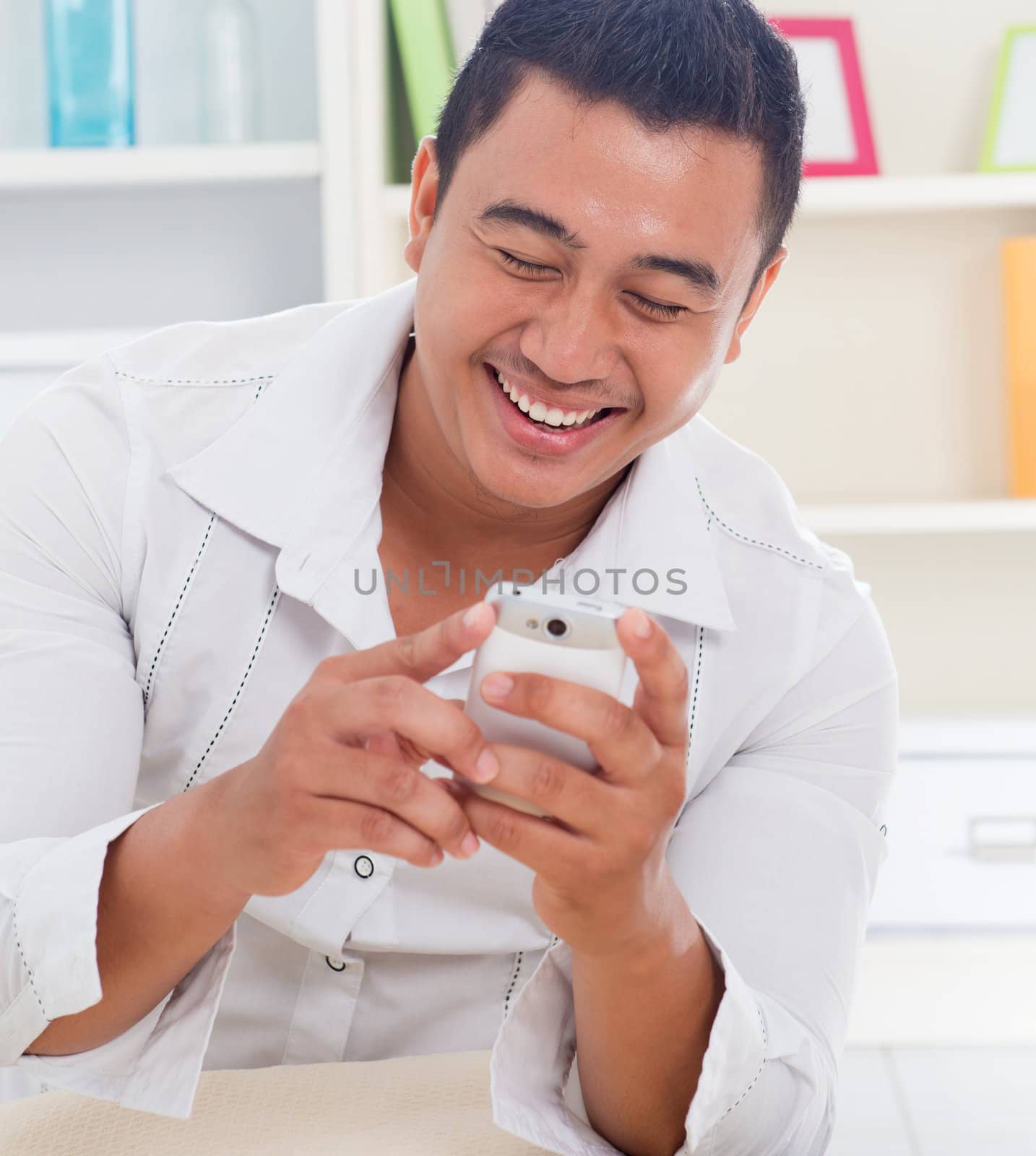 Cheerful Asian man using smartphone at home, looking on screen.