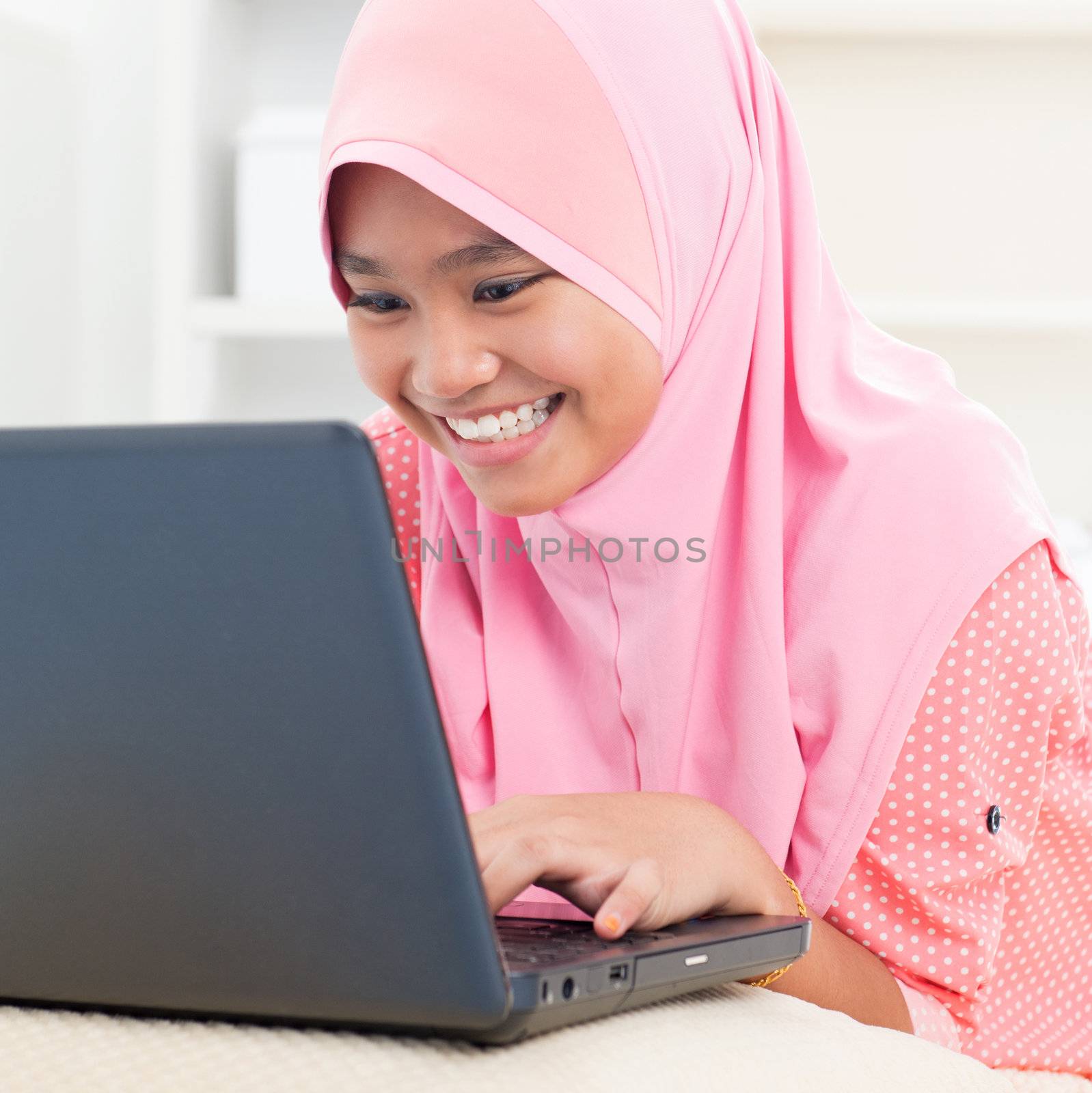 Southeast Asian teenager using notebook at home. Muslim female teen.