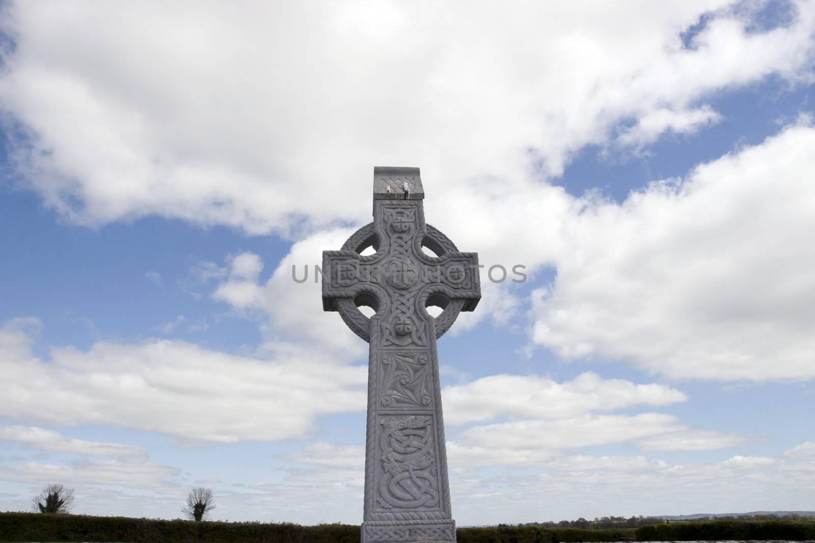 an old celtic cross in an irish graveyard with blue cloudy sky and countryside